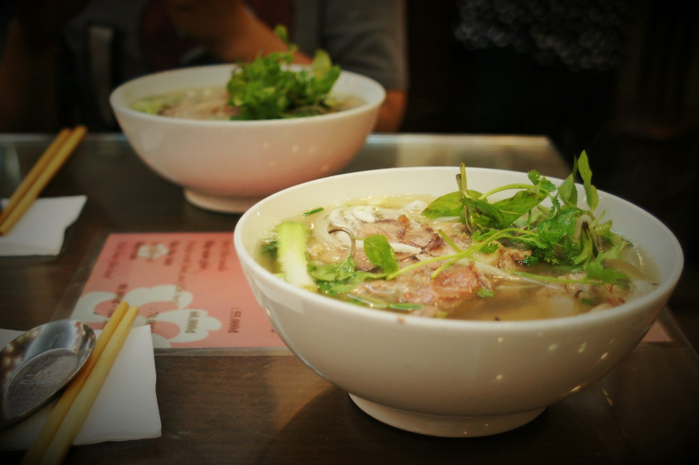 Two steaming bowls of pho on a restaurant table.